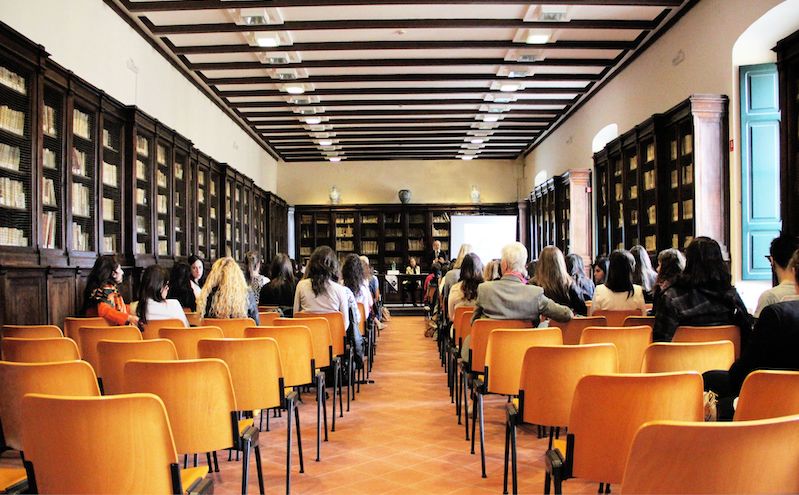 A group of people sitting on wooden chairs watching a presentation.