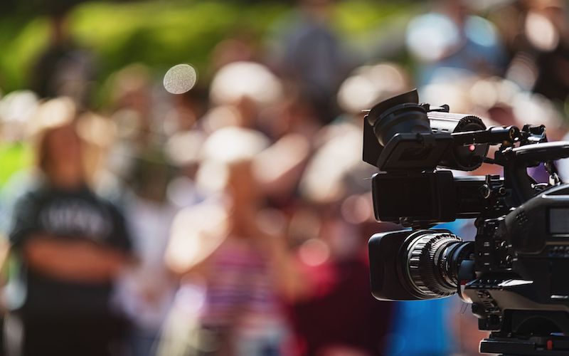 A videocamera facing a large crowd.