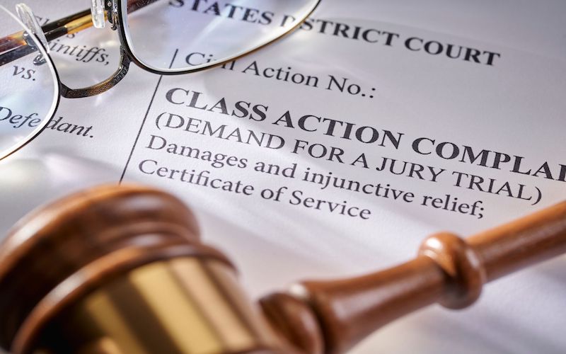 A gavel and pair of eyeglasses laying on top of paperwork titled 'Class Action'