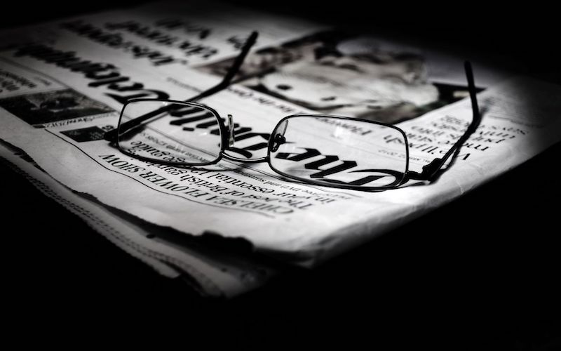 A pair of eyeglasses sitting on top of a newspaper.