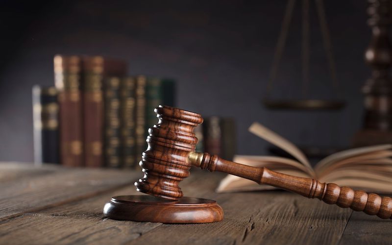 Gavel on a table. On the background is an open book and a row of bookspines.