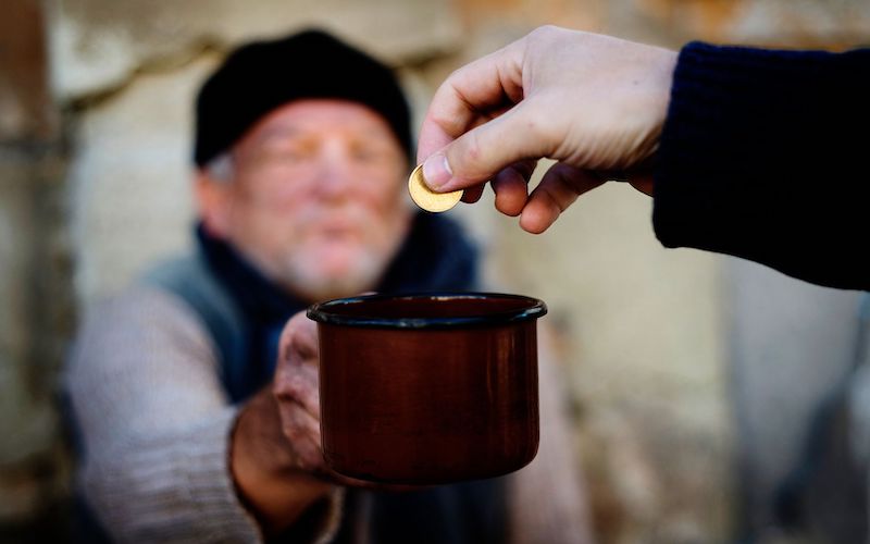 Blurred in the background is the image of panhandler holding out a mug and hand giving him a coin.