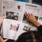 An image of an open newspaper held up by two women, one of which is pointing to a headline.