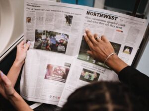 An image of an open newspaper held up by two women, one of which is pointing to a headline.